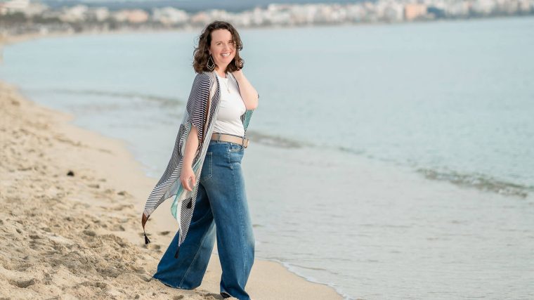 Foto einer Frau am Strand die in die Kamera lächelt