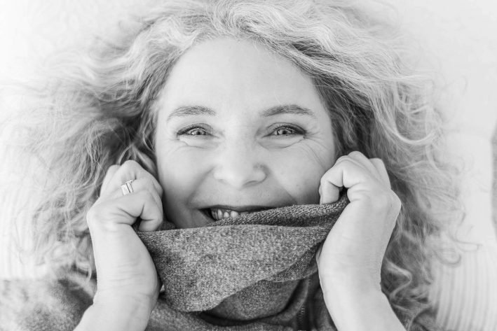Foto einer glücklichen Frau, die mit einem Lächeln ihren Pullover hält.
